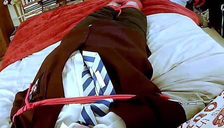 Man in adult school uniform tightly bound and gagged on bed