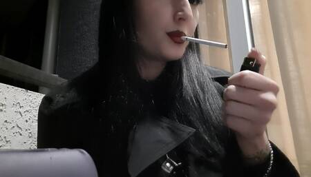 Dominatrix Nika smokes a cigarette on the balcony. Mistress sexy red lips blow smoke in your face