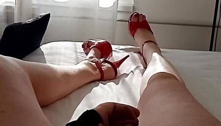 A lying down MILF tranny shows off her long bare legs in red heels and masturbates