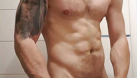 Muscular guy is showing muscle in bathroom and cleaning body