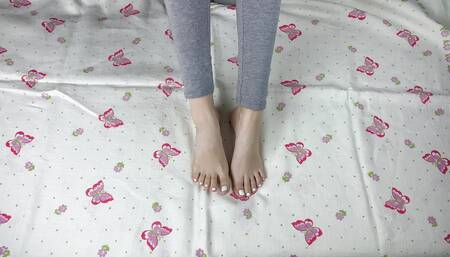 Girl in gray leggings with long legs caresses her feet with a white pedicure