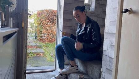 Smoking at the door in leather jacket, jeans and sneakers