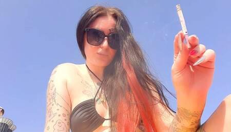 Smoking fetish. Dominatrix smokes a cigarette on the beach