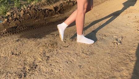 A girl in white socks walks along a dusty road and then she plunges them into the mud where they get dirty entirely