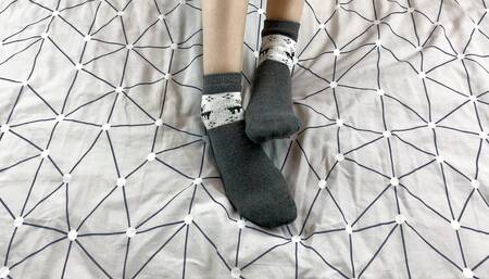 Girl with long legs caresses her feet in gray New Year socks with deer